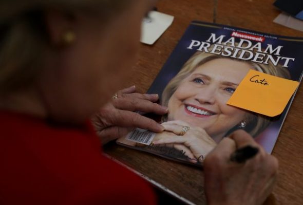 Caption: Hillary Clinton signs a copy of Newsweek’s “Madam President” before she lost to Donald Trump. Photo Credit: GrettyImages 